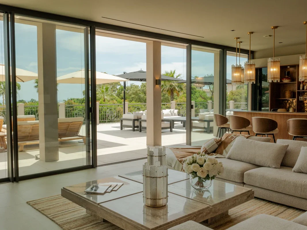 Salon ouvert sur grande terrasse avec mobilier extérieur, palmiers et mer visible en arrière-plan